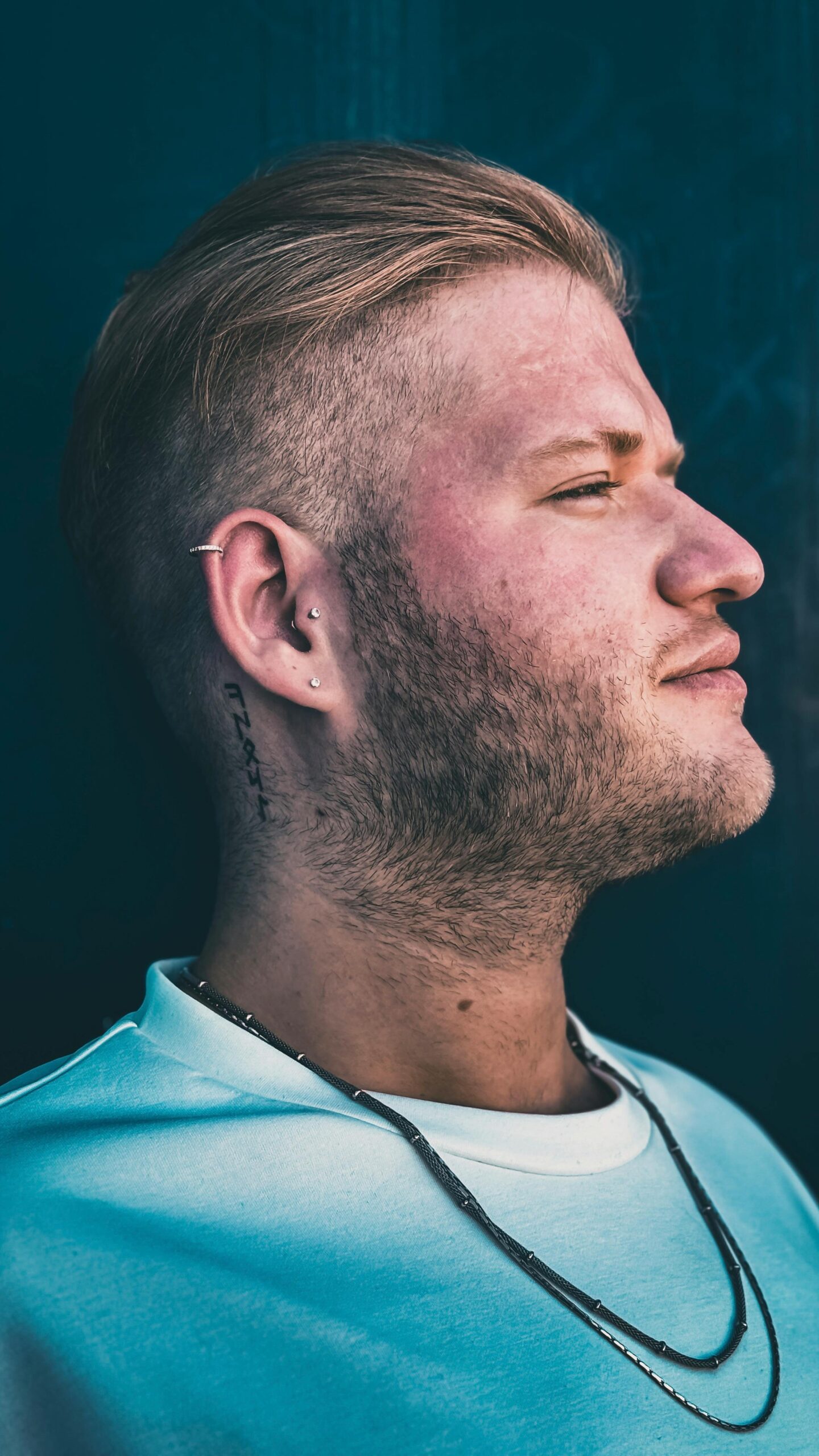 Close-up profile of a stylish young man with earrings against a dark background.