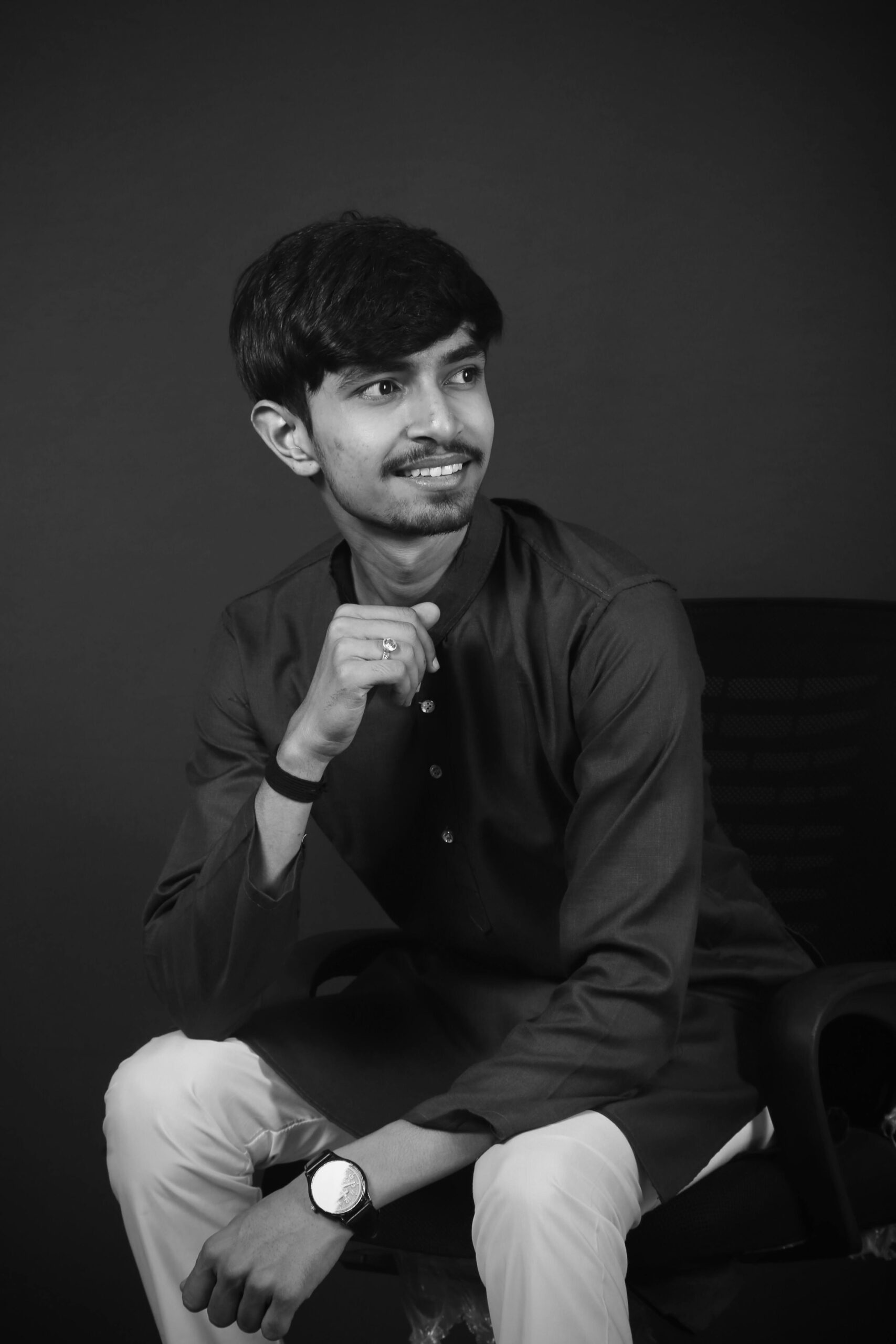 Black and white portrait of a smiling man in traditional kurta sitting indoors.